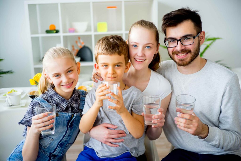 Gezin met twee kinderen drinkt samen een glas gefilterd kraanwater thuis