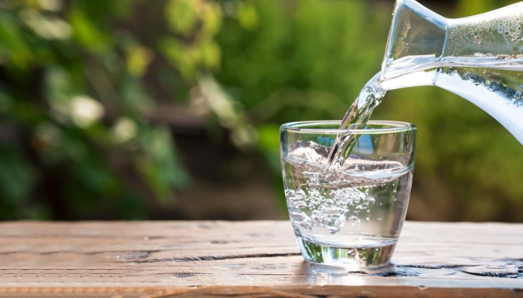 Helder gefilterd water wordt ingeschonken in een glas op een houten tafel