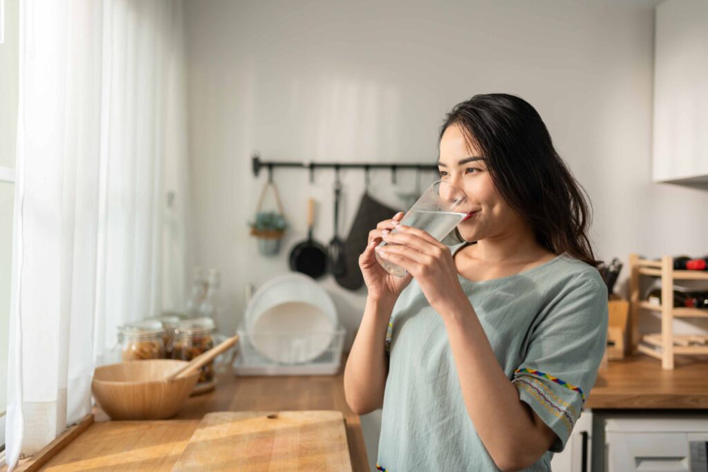 Vrouw drinkt een glas fris kraanwater in een lichte, moderne keuken